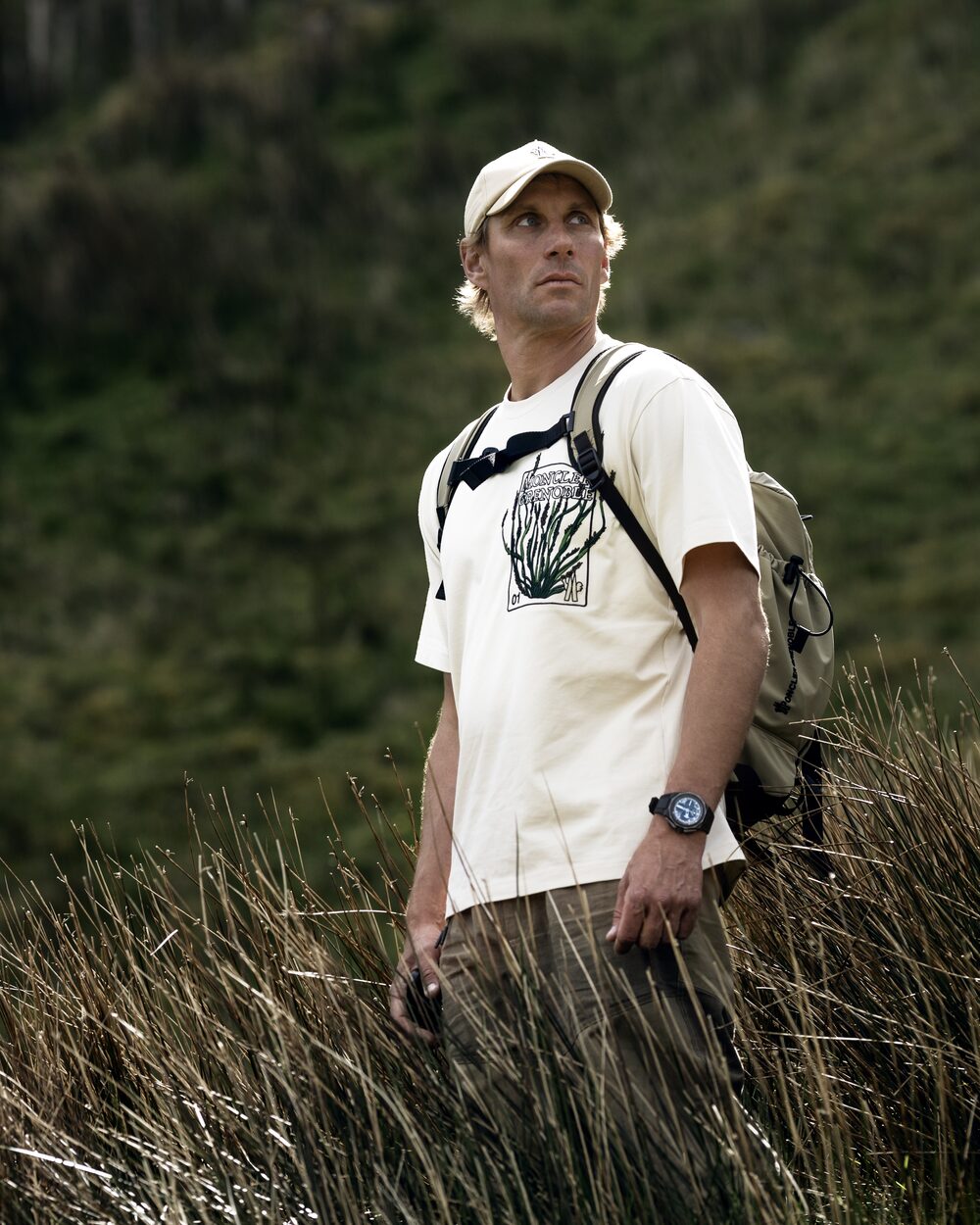 Portrait of Richard Permin in a Moncler tee, standing in tall grass under soft overcast light